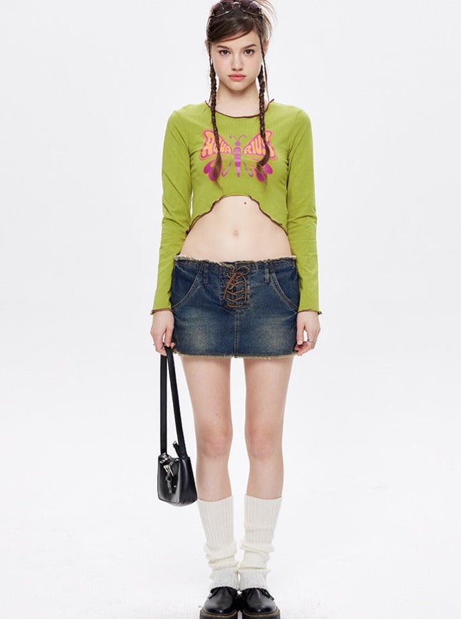 Young woman in green crop top and denim mini skirt, holding a black handbag. Fashionable outfit with knee-high socks and black shoes. Studio background.