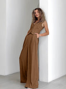 Woman in a stylish brown pinstripe jumpsuit leaning against a white wall, showcasing modern fashion trends and elegant casual wear.