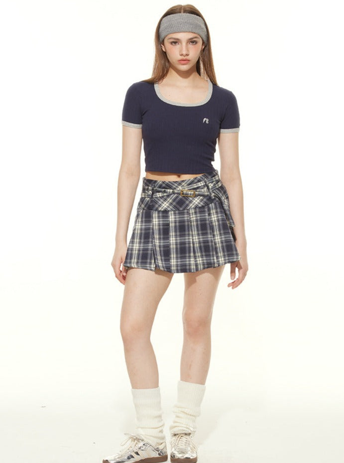 Young woman in a navy crop top and plaid skirt, wearing a headband and leg warmers, showcasing trendy casual fashion.