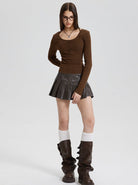 Woman in brown long-sleeve top, black pleated mini skirt, knee-high brown boots, and glasses. Fashionable fall outfit, stylish women's clothing.