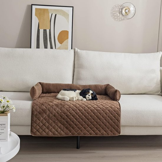 Brown quilted dog bed on a white sofa with a plush toy dog, modern wall art, and a decorative light fixture; stylish pet furniture.