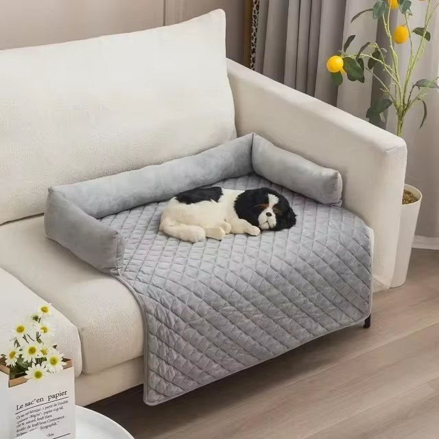 Dog bed on a sofa with a Cavalier King Charles Spaniel, featuring a quilted gray cover and bolster design, perfect for pet comfort and home decor.