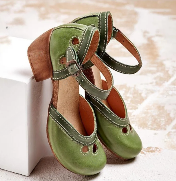 Green leather Mary Jane shoes with wooden block heels, featuring decorative cutouts and white stitching, displayed on a textured surface.