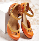 Vintage-style orange leather toddler shoes with ankle straps and cut-out details, displayed on a textured surface. Perfect for children's fashion.