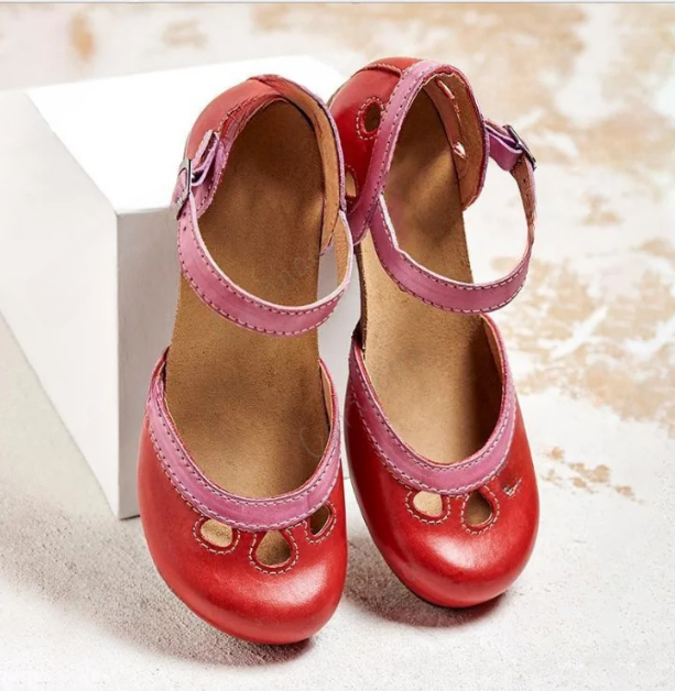 Red leather toddler Mary Jane shoes with pink straps, decorative cutouts, and a soft brown insole, displayed on a white textured surface.