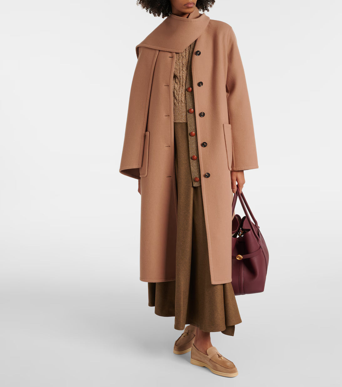 Woman wearing a stylish camel wool coat with oversized collar, brown skirt, and tan loafers, holding a burgundy leather handbag. Fashionable fall outfit.