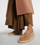 Beige suede loafers with gold buckle detail, worn with a brown skirt and camel coat. Stylish women's footwear, luxury fashion, elegant design.