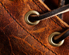 Close-up of brown leather shoe with brass eyelets and black laces, showcasing detailed texture and craftsmanship. Fashion accessory, footwear detail.