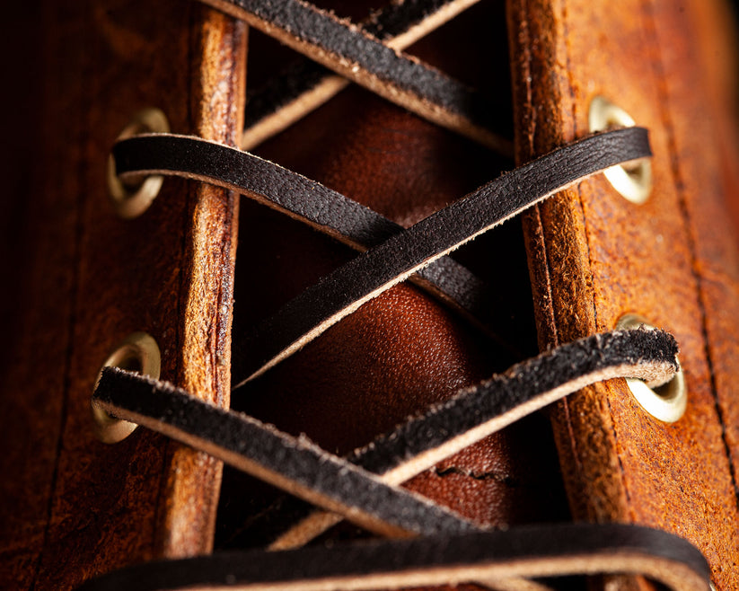 Close-up of brown leather boot with black laces threaded through metal eyelets, showcasing detailed craftsmanship and rugged footwear design.