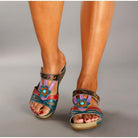 Colorful women's sandals with floral design, featuring blue, red, and purple straps, worn on feet with painted toenails. Fashionable summer footwear.