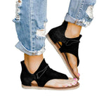 Black open-toe sandals with ankle support worn with ripped blue jeans. Stylish summer footwear, casual fashion, women's shoes.