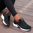 Black mesh athletic sneakers with white soles on wooden deck; stylish, breathable running shoes for women; comfortable sports footwear.