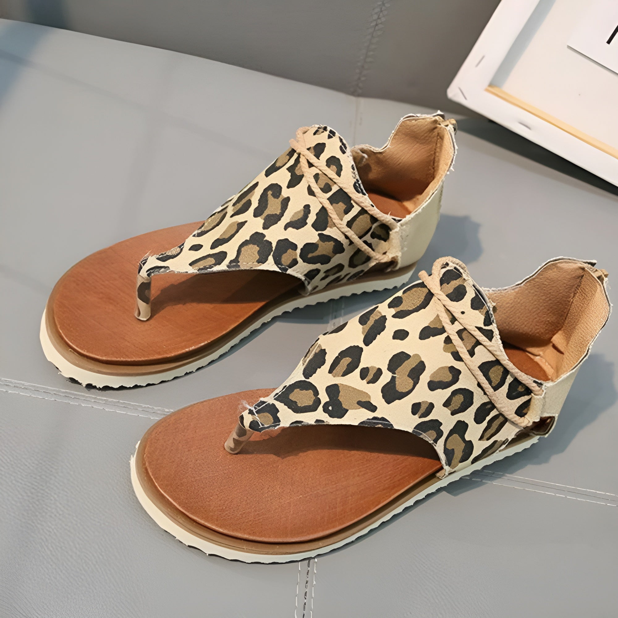 Leopard print sandals with open toe design, cushioned footbed, and adjustable ankle strap on a gray surface. Stylish women's summer footwear.