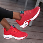 Red athletic sneakers with white soles and air cushioning, worn by a person on a wooden floor. Stylish, comfortable footwear for running or casual wear.