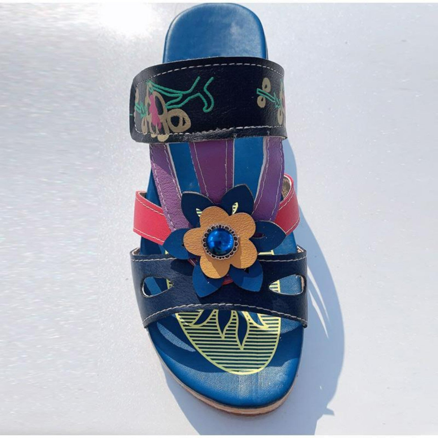 Colorful women's sandal with floral design, featuring a blue gemstone accent, multicolored straps, and artistic patterns. Fashionable summer footwear.