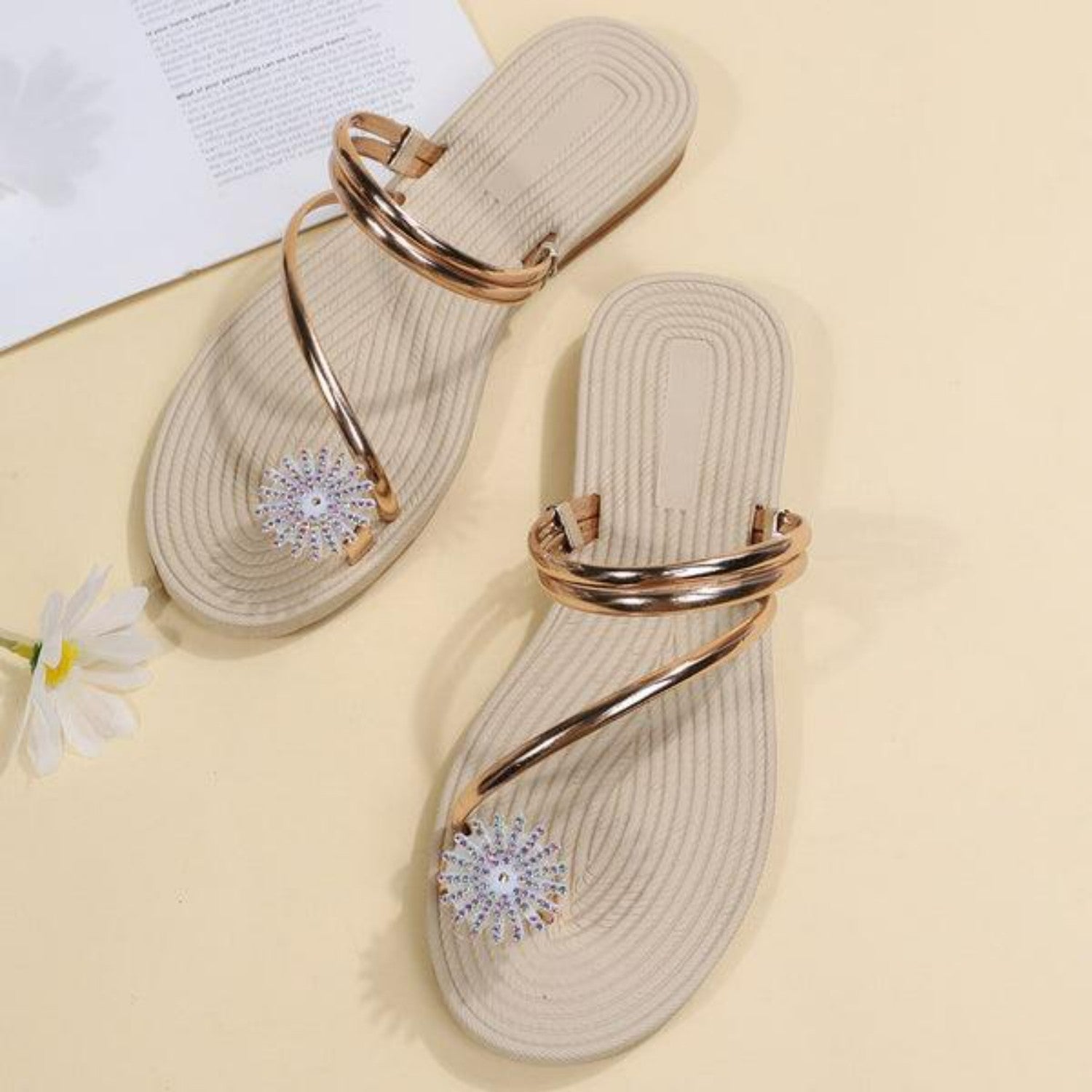 Beige flat sandals with gold straps and floral rhinestone accents on a light background, perfect for summer fashion and casual wear.