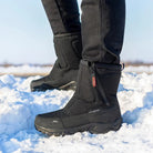 Black winter boots with rugged soles on snow, featuring a zipper closure and insulated design for warmth. Ideal for outdoor activities in cold weather.