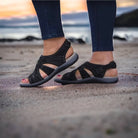 Black strappy sandals on a beach at sunset, featuring comfortable soles and stylish design. Perfect for summer fashion and casual outdoor wear.