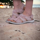 Comfortable pink leather sandals on sandy beach at sunset, featuring adjustable straps and cushioned soles. Perfect for summer travel and casual wear.