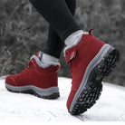 Red winter hiking boots with durable soles, worn by a person walking on snow. Ideal for outdoor activities, providing warmth and traction.