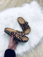 Leopard print sandals with cork soles on white faux fur rug, featuring bow detail. Perfect for casual summer fashion and comfortable footwear trends.