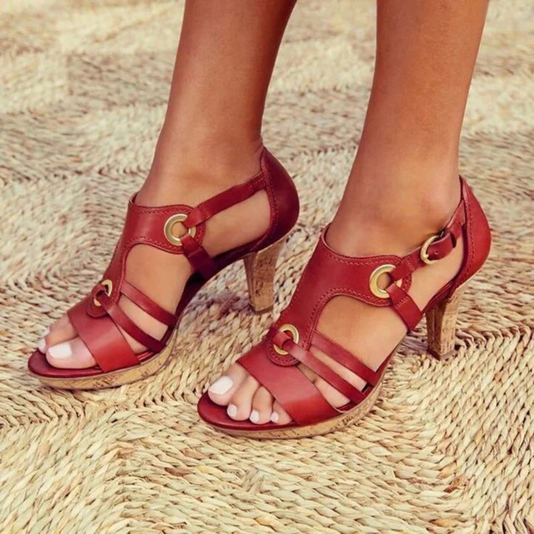 Red leather high-heeled sandals with gold buckle accents on woven straw mat. Stylish women's footwear, perfect for summer fashion and casual outings.