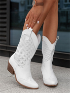 White breathable cowboy boots with perforated design, wooden heel, and pointed toe, worn by a person with a watch. Fashionable footwear for women.