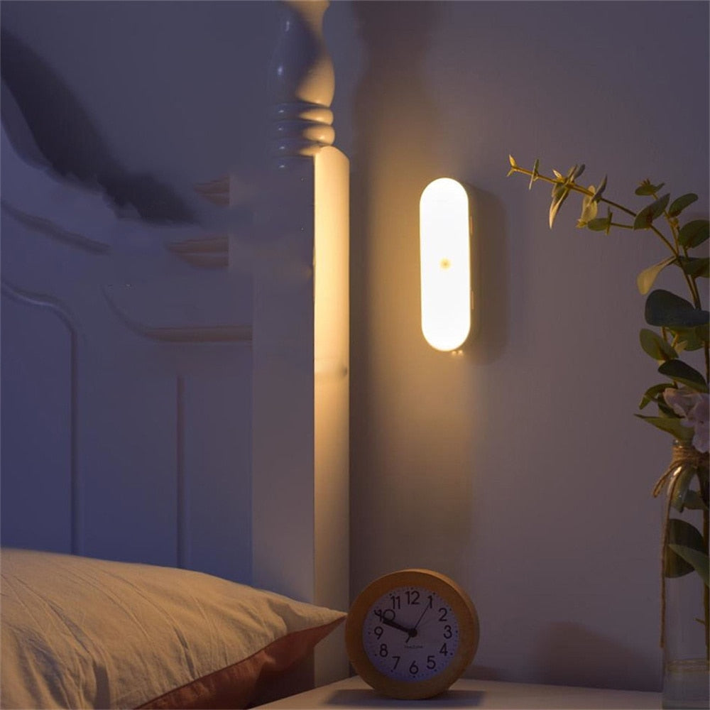 Wall-mounted LED night light illuminating a cozy bedroom with a wooden analog clock and a plant on a bedside table. Perfect for ambient lighting.