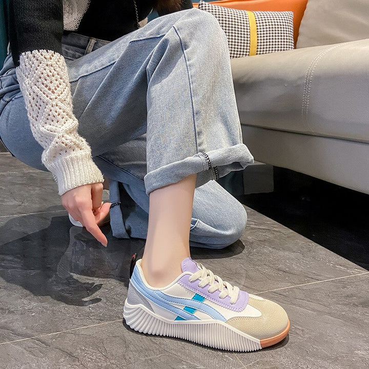 Casual sneaker with pastel purple and beige accents on a woman's foot, paired with rolled-up jeans, showcasing trendy footwear fashion indoors.