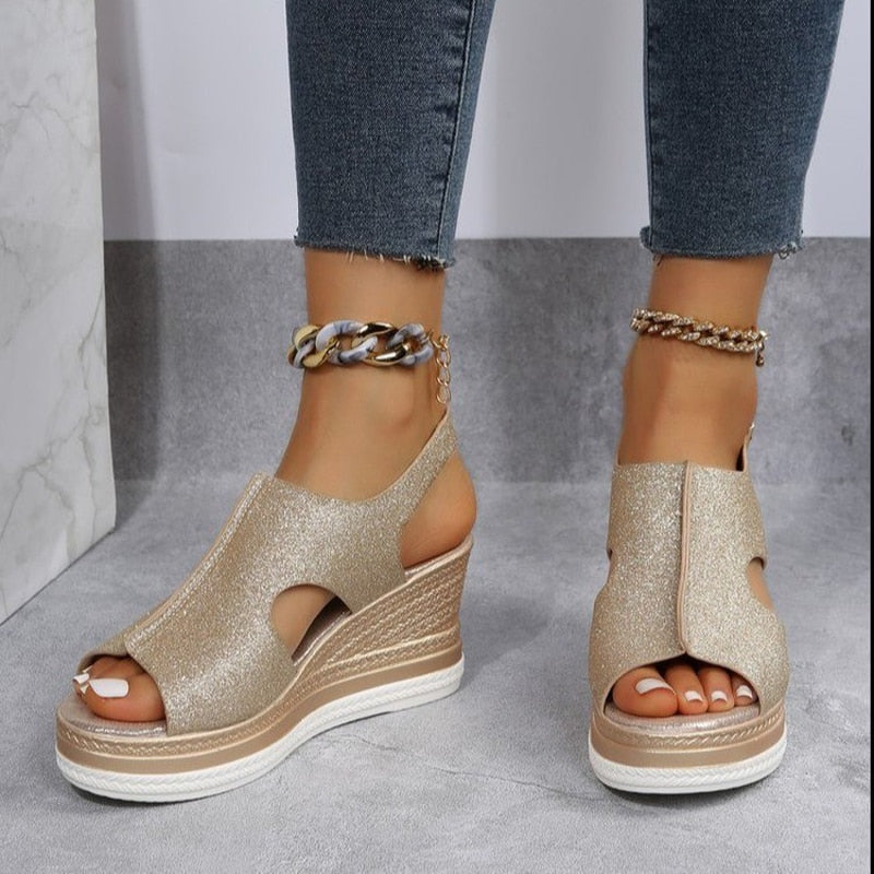 Gold glitter wedge sandals with open toe design, paired with ankle chain accessories. Stylish women's footwear, perfect for summer fashion trends.