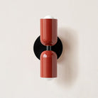 Modern red wall sconce with dual cylindrical lights on a black base, minimalist design, perfect for contemporary home lighting decor.