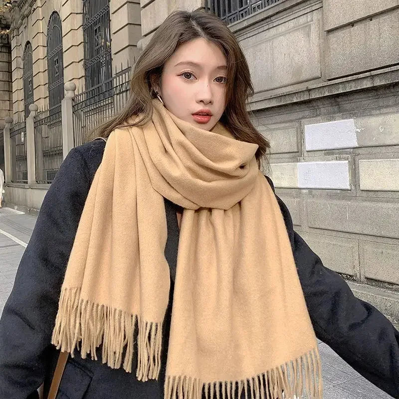 Woman wearing a stylish oversized beige scarf and black coat, standing outdoors. Fashionable winter outfit, street style, cozy accessories.