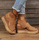 Women's tan wedge sandals with cutout design, ankle strap, and espadrille platform. Paired with distressed denim jeans on wooden floor background.