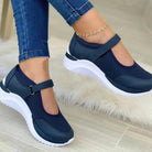 Women's navy blue Mary Jane sneakers with white soles, mesh upper, and adjustable strap, paired with jeans. Stylish casual footwear for comfort.