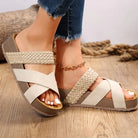 Women's beige woven platform sandals with crisscross straps, paired with frayed hem jeans. Stylish summer footwear on wooden floor background.