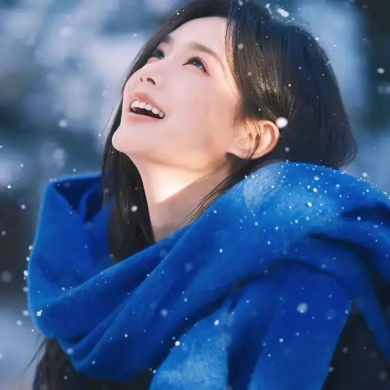 A person in a blue scarf looks up joyfully amidst falling snowflakes, capturing a serene winter moment. Winter fashion, joyful expression, snow scene.