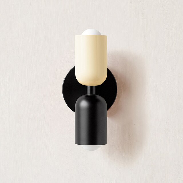 Modern minimalist wall sconce with black and beige cylindrical design, featuring dual light bulbs. Ideal for contemporary home lighting decor.