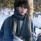 I don't know who this is, but the image shows a person in a blue coat and gray scarf standing outdoors in a snowy landscape, leaning against a tree.