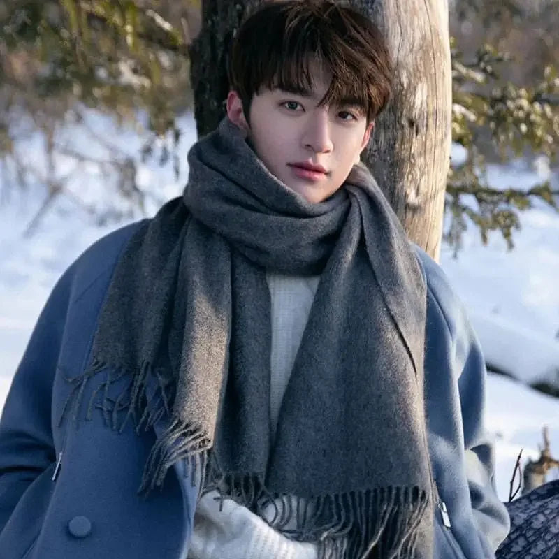 I don't know who this is, but the image shows a person in a blue coat and gray scarf standing outdoors in a snowy landscape, leaning against a tree.