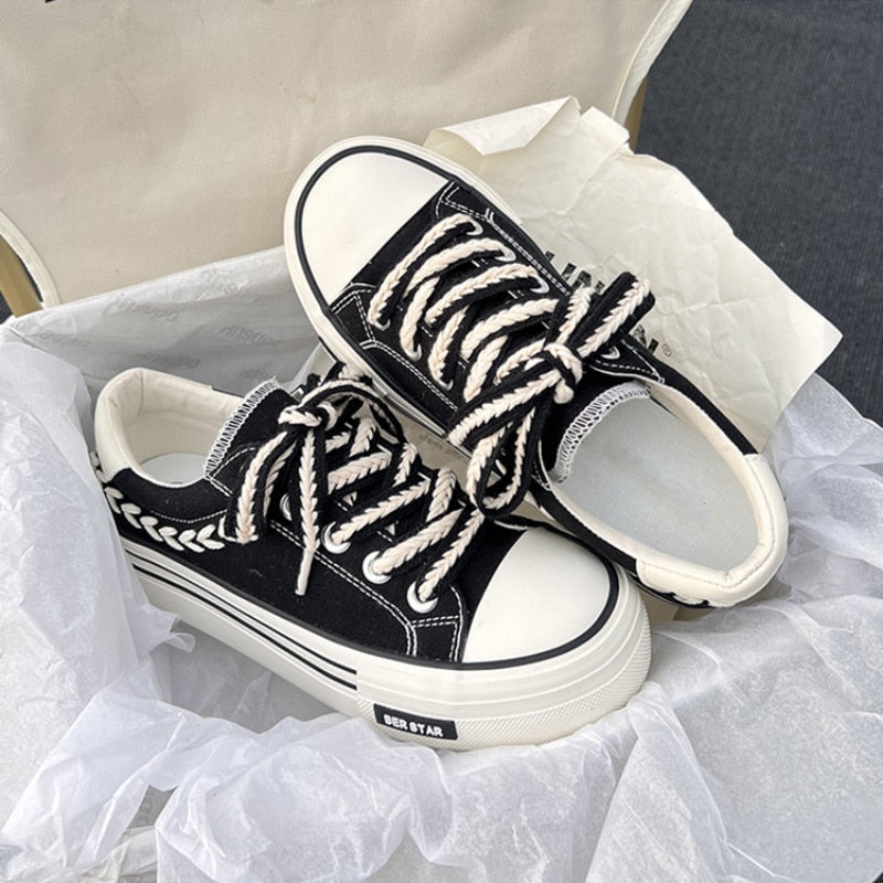 Black and white canvas sneakers with braided laces and leaf embroidery, displayed in a shoebox. Trendy casual footwear, stylish design.