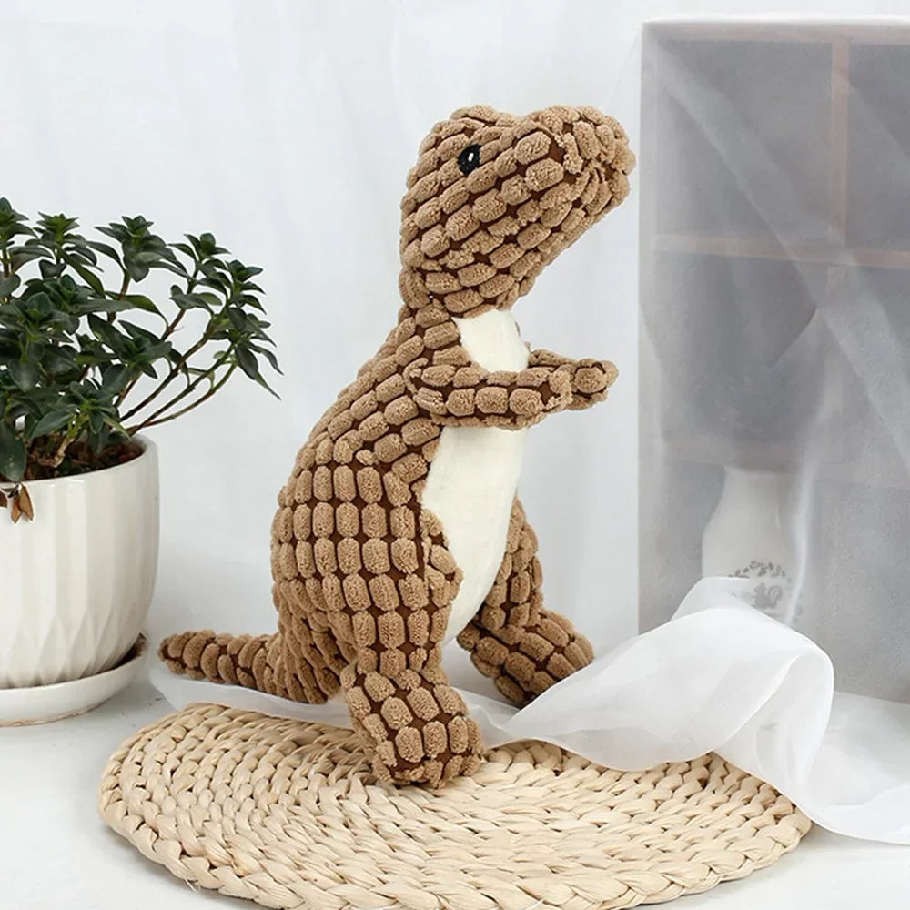 Plush dinosaur toy with textured brown fabric, standing on a woven mat beside a potted plant, perfect for kids' room decor or gifts.