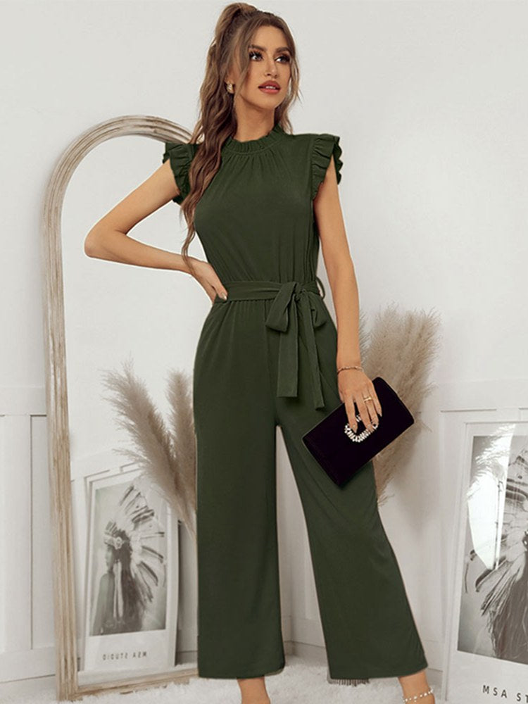 Woman in elegant green jumpsuit with ruffled sleeves, holding a black clutch. Fashionable outfit for formal occasions. Stylish women's clothing.