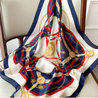Elegant silk scarf with intricate gold chain and belt pattern, featuring navy, red, and white colors, draped over a chair. Fashion accessory.