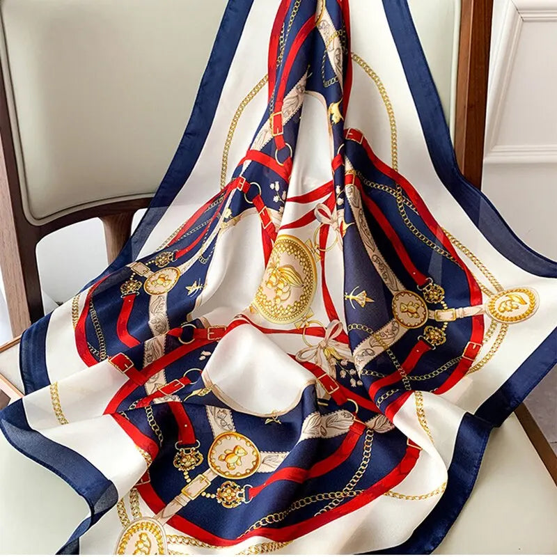 Elegant silk scarf with intricate gold chain and belt pattern, featuring navy, red, and white colors, draped over a chair. Fashion accessory.