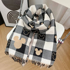 Plaid scarf with black and beige Mickey Mouse pattern on a white chair, perfect for cozy winter fashion. Stylish accessory for Disney fans.