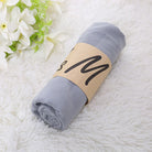 Gray muslin swaddle blanket rolled on white fluffy rug with floral decor; soft baby wrap, newborn essentials, nursery accessory.