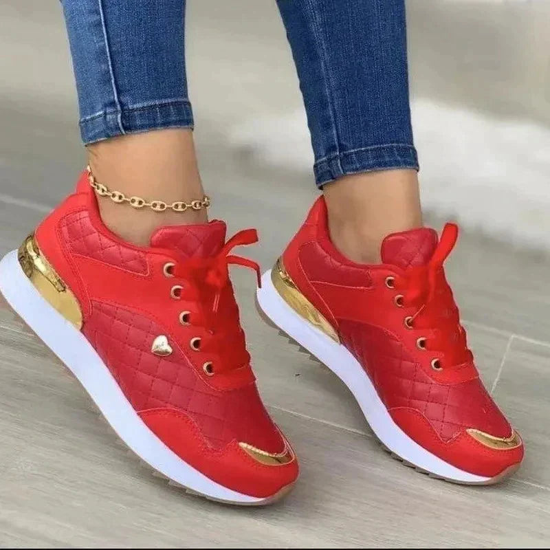 Red and gold women's sneakers with quilted design, white soles, and metallic accents, paired with blue jeans. Fashionable casual footwear.