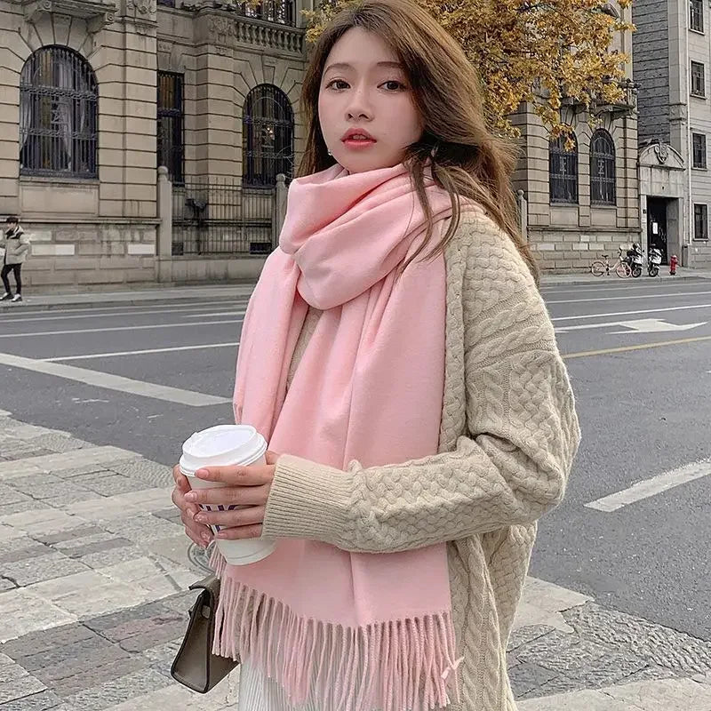 Woman in cozy beige sweater and pink scarf holding coffee cup on city street; fall fashion, urban style, warm clothing, autumn outfit.