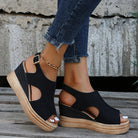 Black wedge sandals with open-toe design and ankle strap, paired with frayed hem jeans. Stylish summer footwear for women, perfect for casual outings.