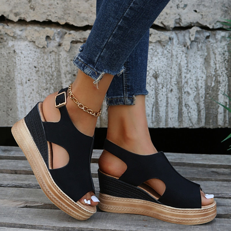 Black wedge sandals with open-toe design and ankle strap, paired with frayed hem jeans. Fashionable summer footwear for women.